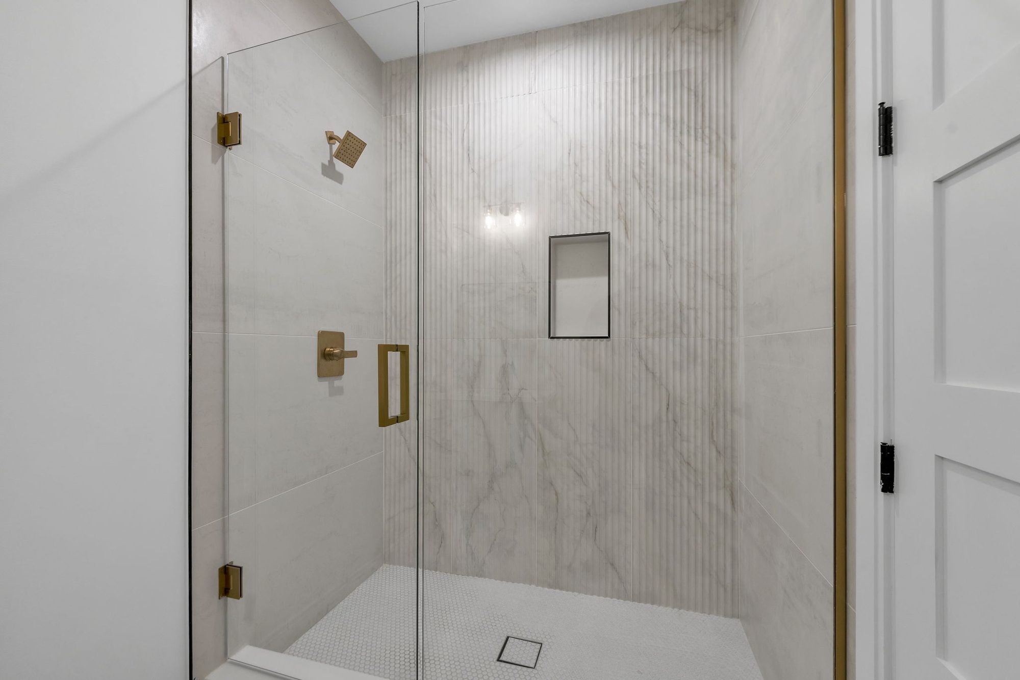 Guest shower with fluted marble-look tile and brass fixtures