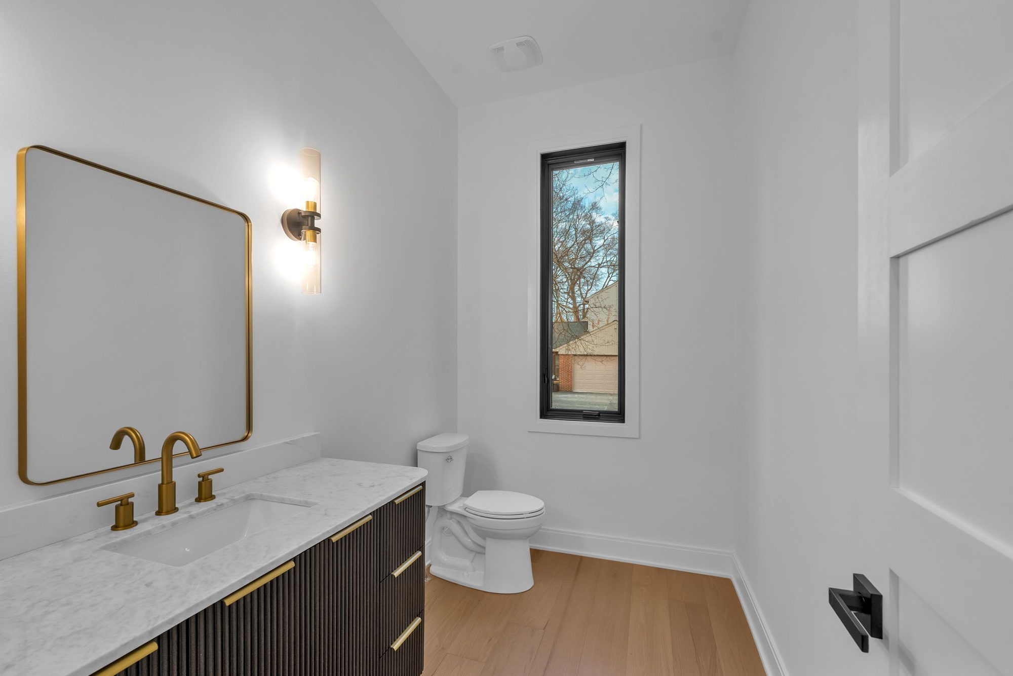 Powder room with dark fluted vanity, marble top and brass faucet