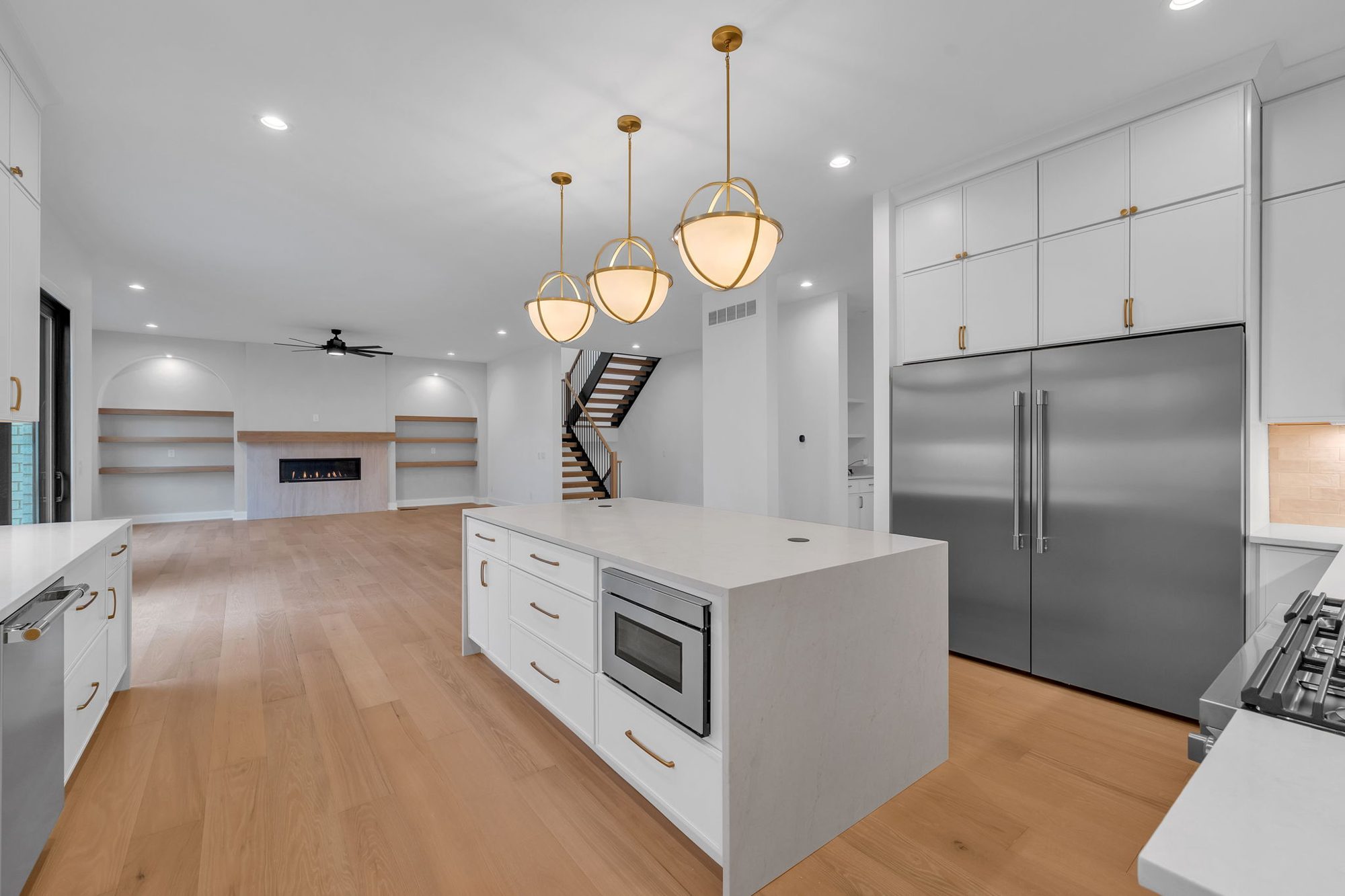 Island with built-in microwave drawer, paneled fridge wall and brass globe pendants