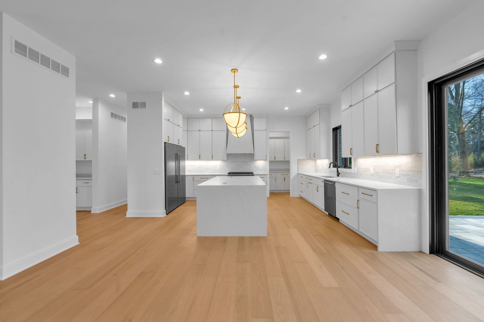 Wide view of white kitchen with marble waterfall island and brass pendants