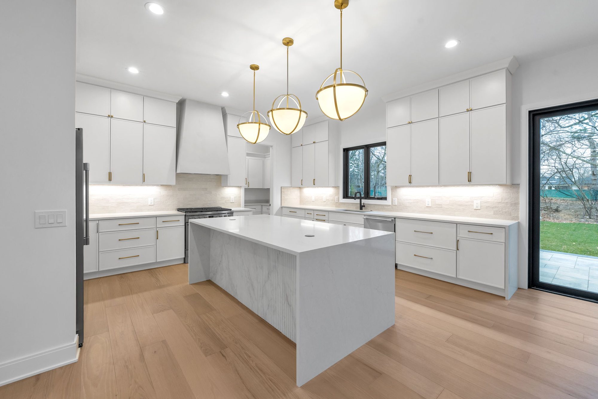 White kitchen with fluted marble waterfall island, plaster hood and brass globe pendants