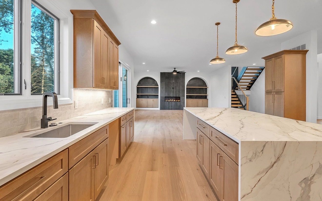 Natural maple kitchen with marble waterfall island and brass pendants