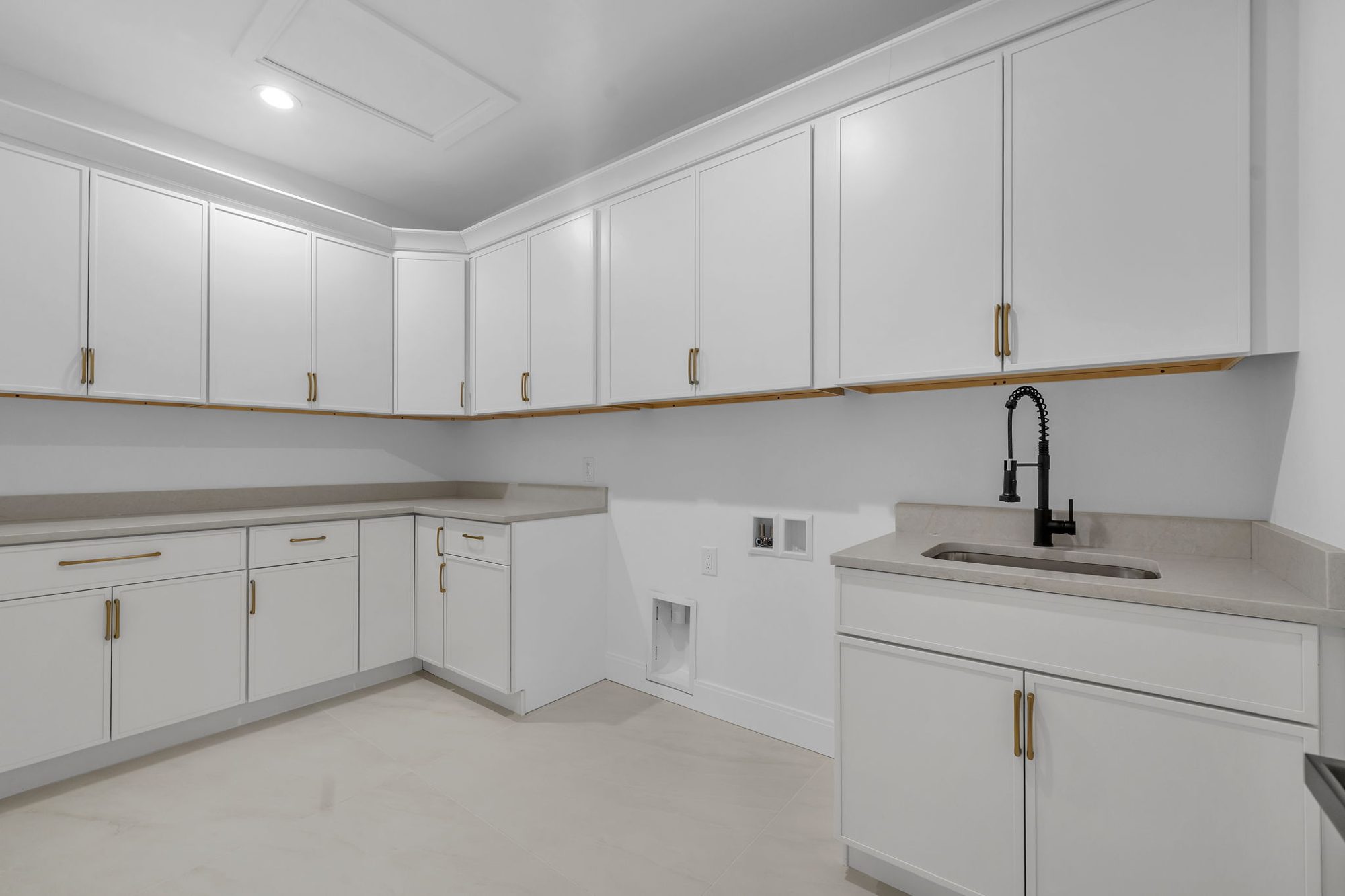 White laundry room cabinetry with brass pulls and utility sink